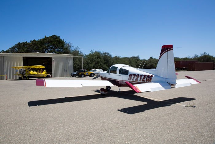 Small red and white low wing aircraft parked on the ramp at Oceano Airport